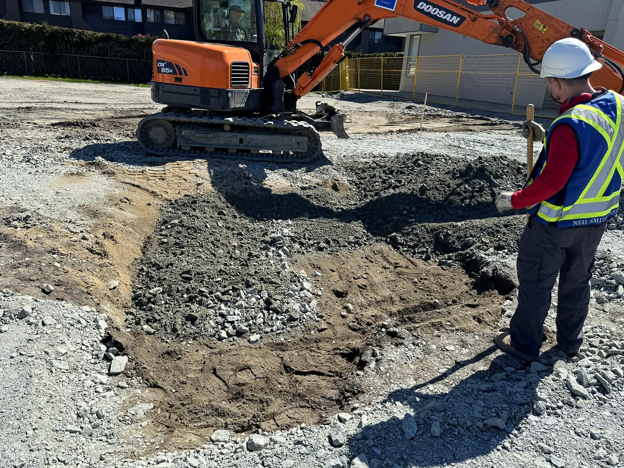 NSC excavator excavating the pad with a crew member checking grade