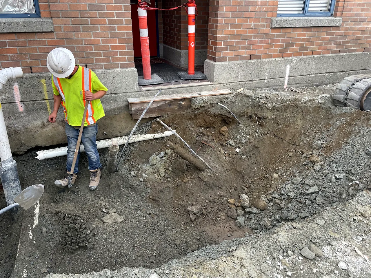 Worker excavating a service trench along the Fire Hall 12 foundation