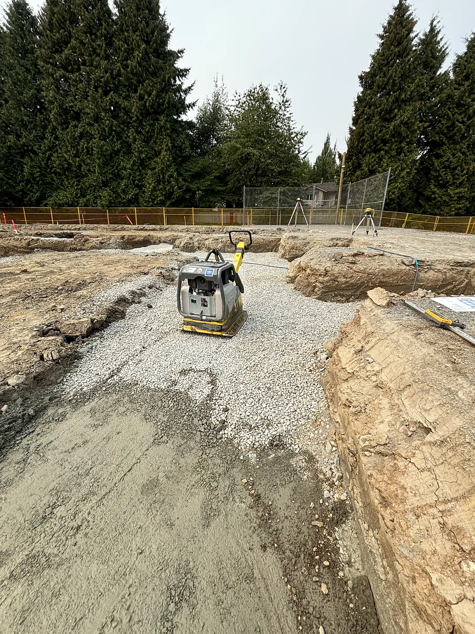 Plate compactor on granular base between excavated footings