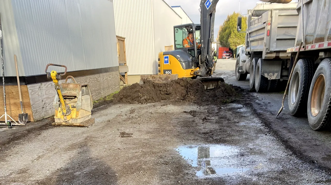 Excavator, plate compactor and trucks preparing the portable pad at James Whiteside Elementary