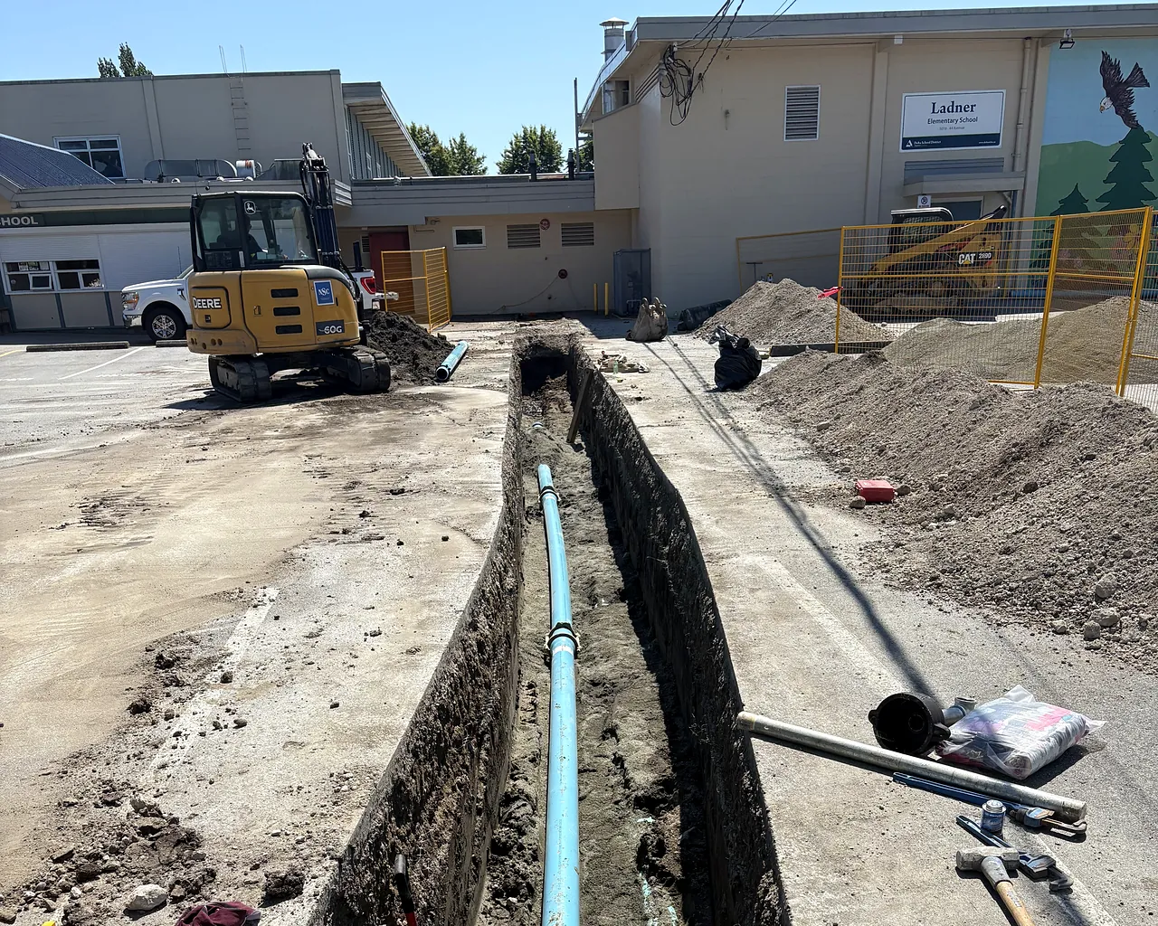 NSC excavator beside an open trench with new water service pipe at Ladner Elementary