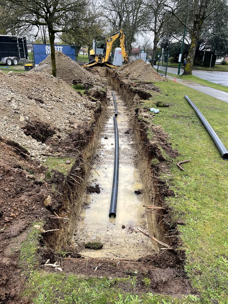 Service trench across Columbia Park with excavator