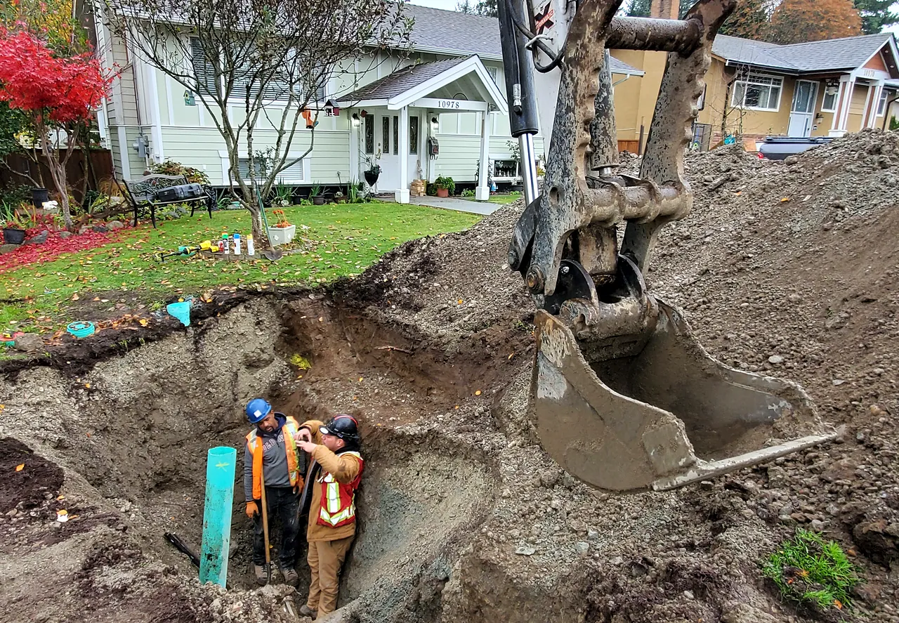 Excavator opening a service trench as crew work in the cut, North Surrey