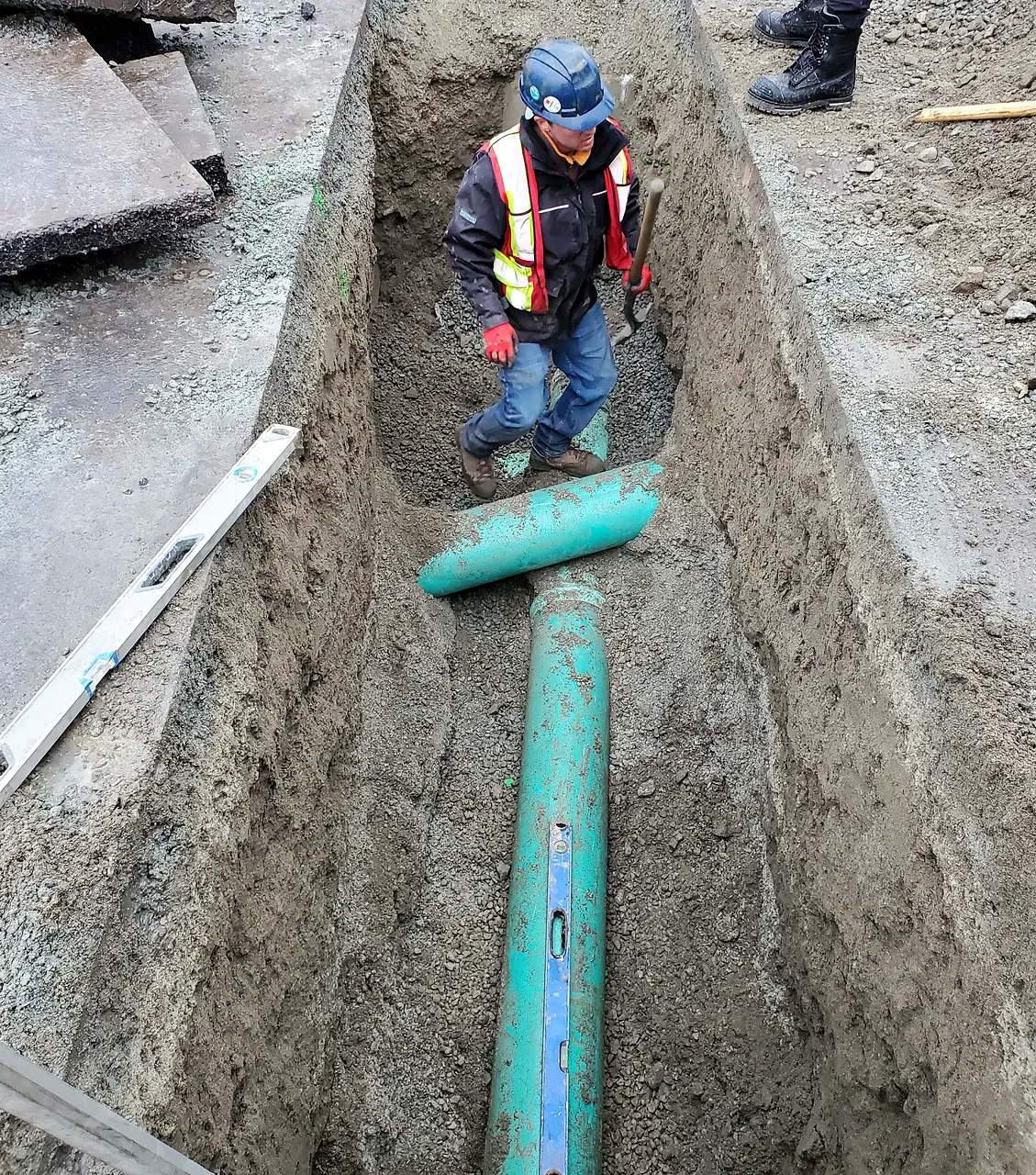 Worker bedding a new PVC sewer pipe in a trench