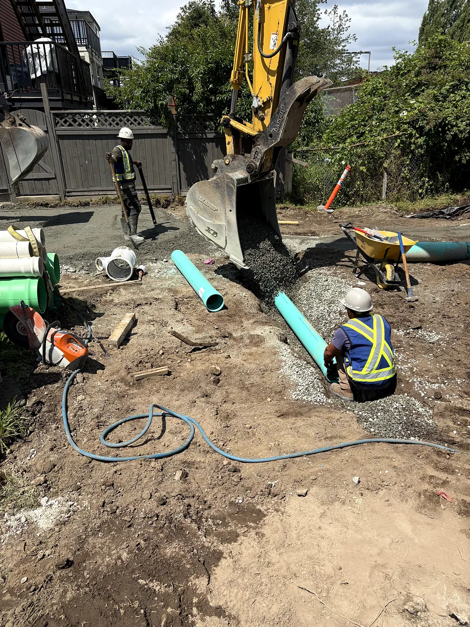 Crew laying PVC sewer pipe as the excavator places bedding