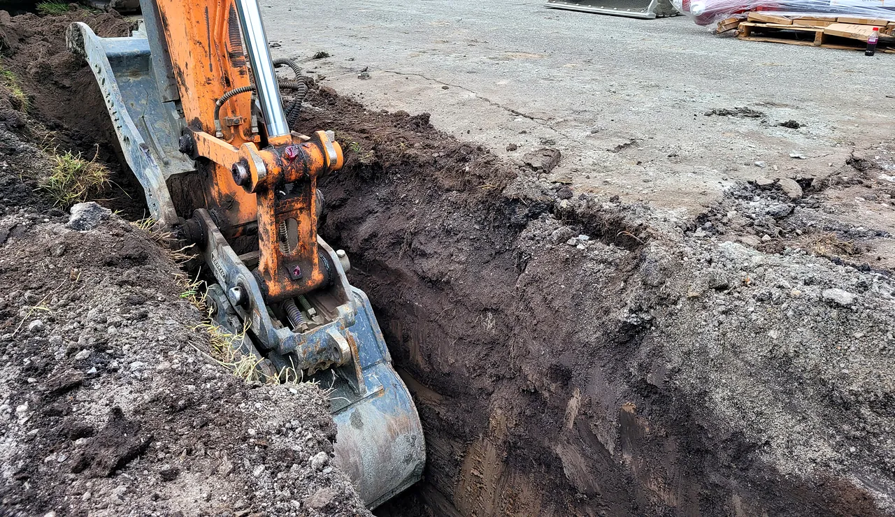 Excavator digging a utility trench beside Tomsett Elementary