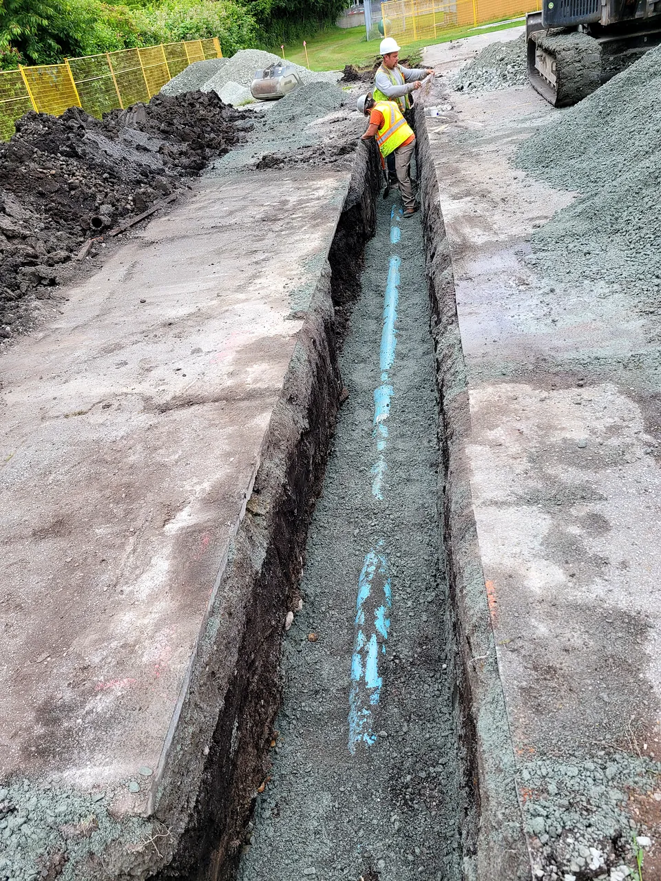 NSC crew in hard hats checking grade on a water service trench at Tomsett Elementary