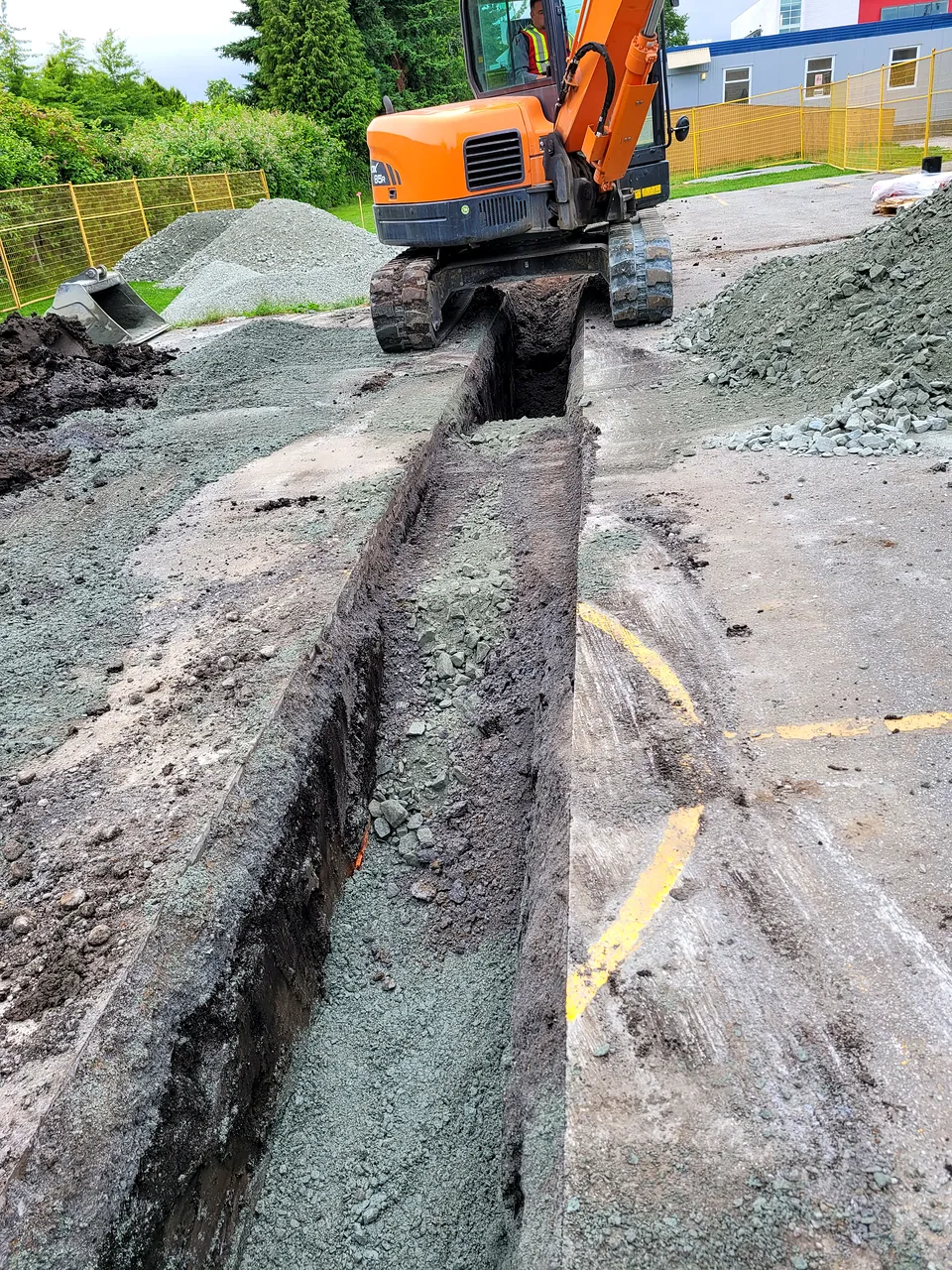 Excavator straddling a bedded water service trench at Tomsett Elementary