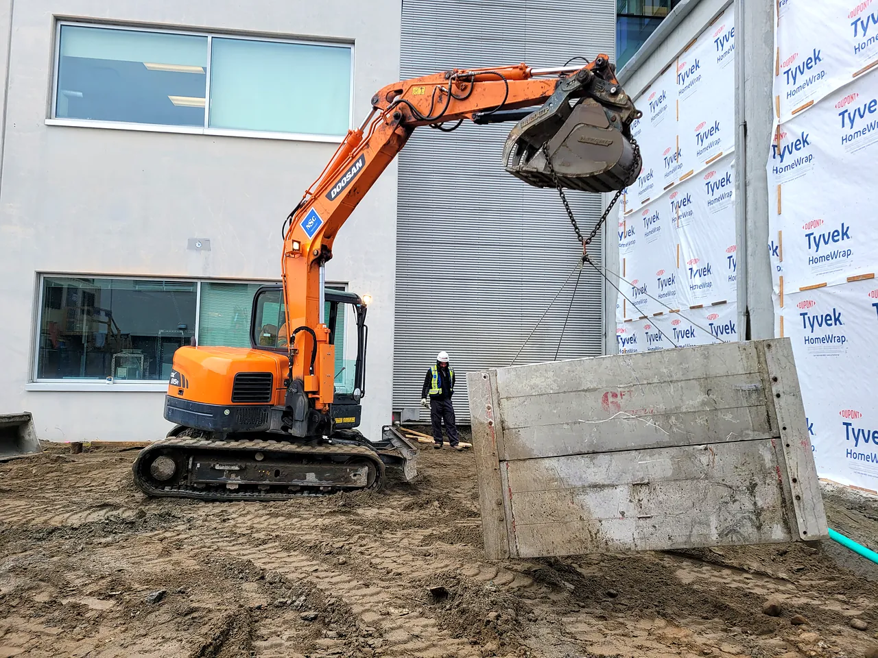 Excavator setting a trench shoring box at UBC